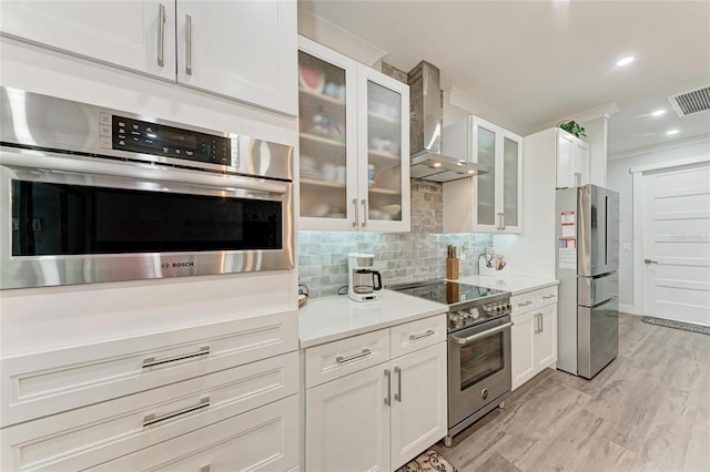 kitchen featuring appliances with stainless steel finishes, white cabinets, wall chimney range hood, and backsplash