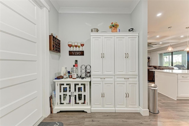 bar with light wood-type flooring, ornamental molding, white cabinets, and hanging light fixtures