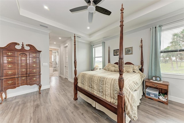 bedroom with ceiling fan, connected bathroom, wood-type flooring, and a raised ceiling