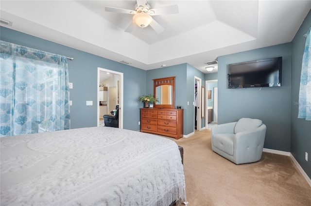 bedroom featuring ceiling fan, ensuite bath, a raised ceiling, and carpet