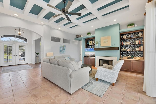 tiled living room with beamed ceiling, french doors, a high ceiling, coffered ceiling, and built in shelves