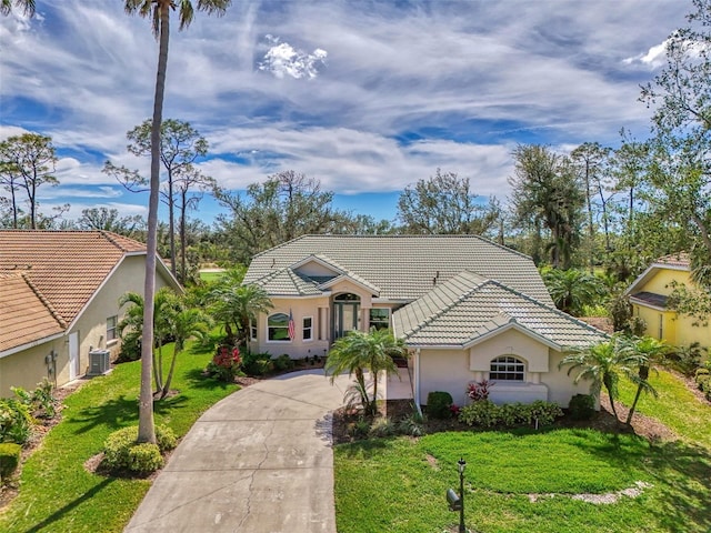 mediterranean / spanish-style house featuring stucco siding, concrete driveway, central AC unit, a tiled roof, and a front lawn