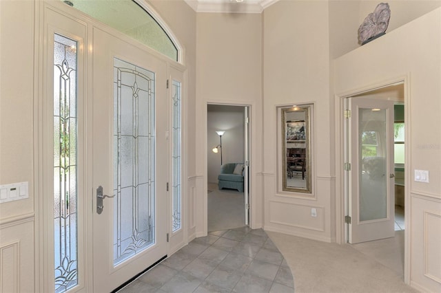 entryway with ornamental molding, a high ceiling, and a decorative wall