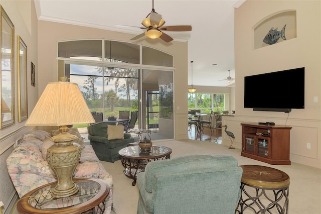 carpeted living area featuring a decorative wall, a sunroom, a ceiling fan, wainscoting, and crown molding