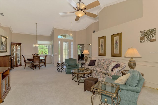 carpeted living area featuring a towering ceiling, visible vents, crown molding, and ceiling fan with notable chandelier