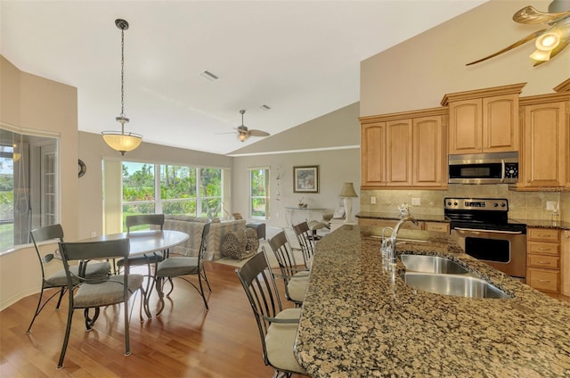 kitchen featuring ceiling fan, open floor plan, appliances with stainless steel finishes, decorative backsplash, and dark stone countertops