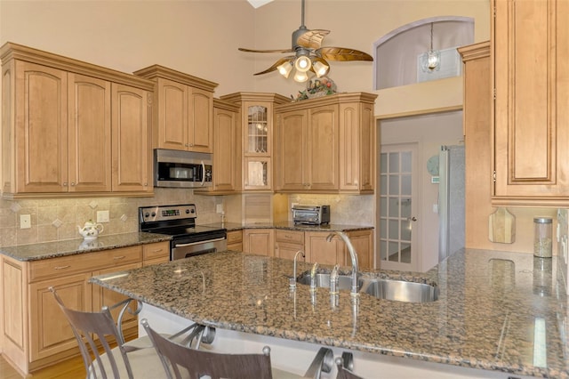 kitchen with tasteful backsplash, dark stone counters, a peninsula, stainless steel appliances, and a sink