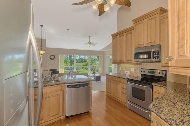 kitchen with light wood finished floors, open floor plan, a sink, stainless steel appliances, and backsplash