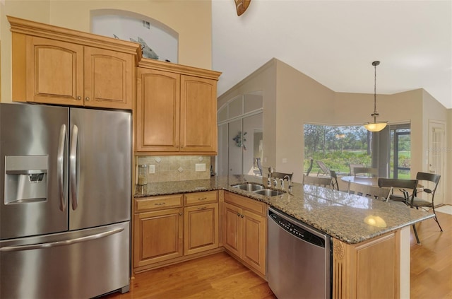 kitchen with stone countertops, a peninsula, stainless steel appliances, light wood-type flooring, and a sink