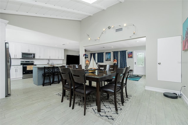 dining room with high vaulted ceiling, beamed ceiling, and light hardwood / wood-style floors