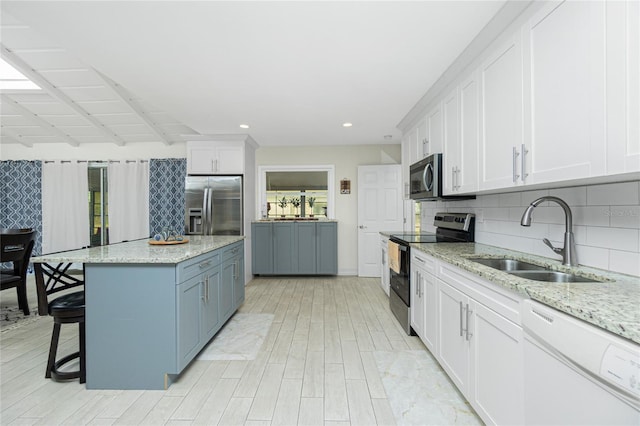 kitchen with white cabinets, stainless steel appliances, a kitchen island, and light stone countertops