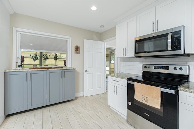 kitchen featuring appliances with stainless steel finishes, white cabinets, tasteful backsplash, and light stone counters