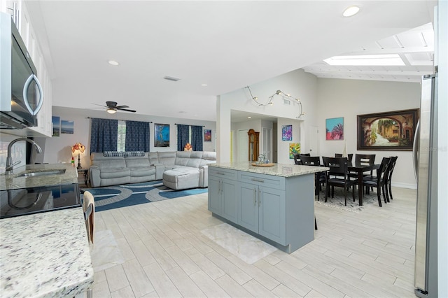 kitchen with light wood-type flooring, sink, lofted ceiling with skylight, light stone counters, and appliances with stainless steel finishes