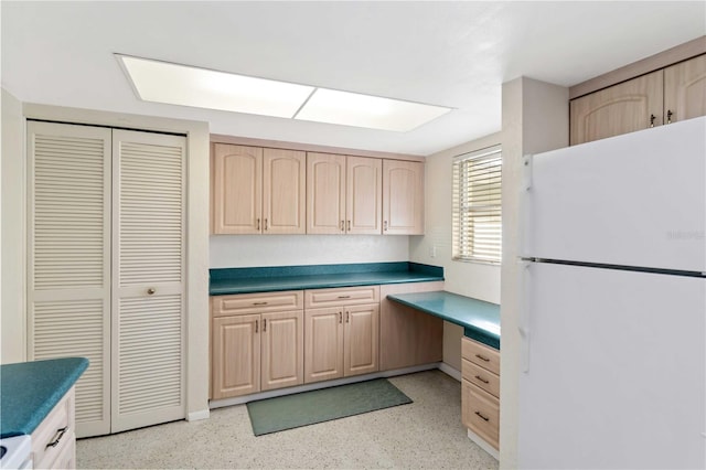 kitchen with white refrigerator, built in desk, and light brown cabinets