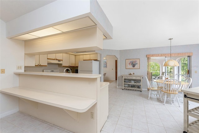 kitchen with freestanding refrigerator, a peninsula, under cabinet range hood, light tile patterned flooring, and light countertops
