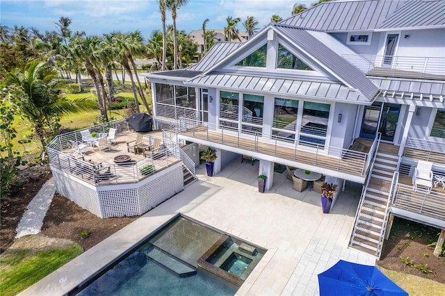 back of property featuring a swimming pool with hot tub, a fire pit, a patio area, a sunroom, and a balcony