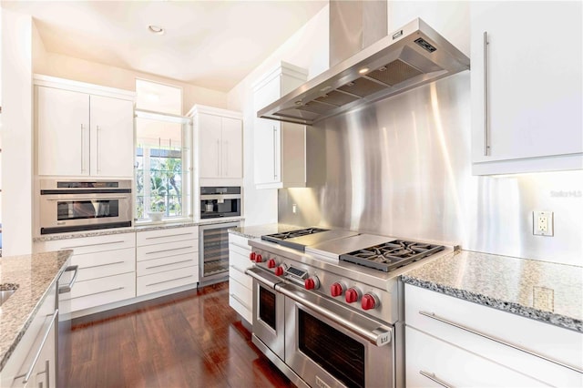 kitchen with stainless steel appliances, dark hardwood / wood-style floors, light stone counters, white cabinets, and wall chimney exhaust hood