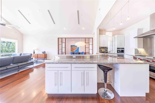 kitchen featuring high end stainless steel range, white cabinetry, pendant lighting, vaulted ceiling with skylight, and a kitchen island with sink