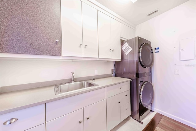 laundry room featuring cabinets, stacked washer and clothes dryer, sink, and light wood-type flooring