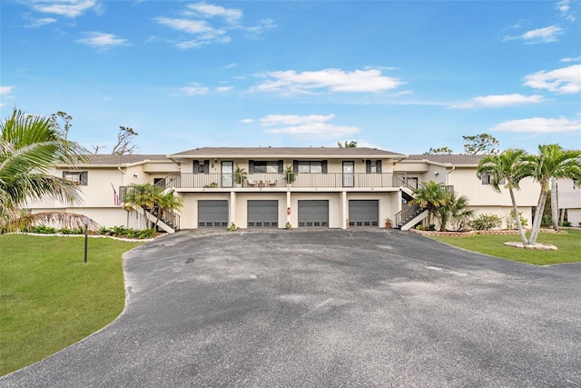 view of front of home with a balcony, aphalt driveway, stairs, a front lawn, and stucco siding