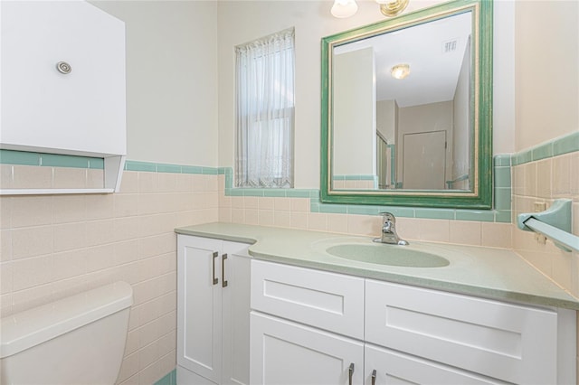 bathroom featuring toilet, vanity, visible vents, tile walls, and wainscoting