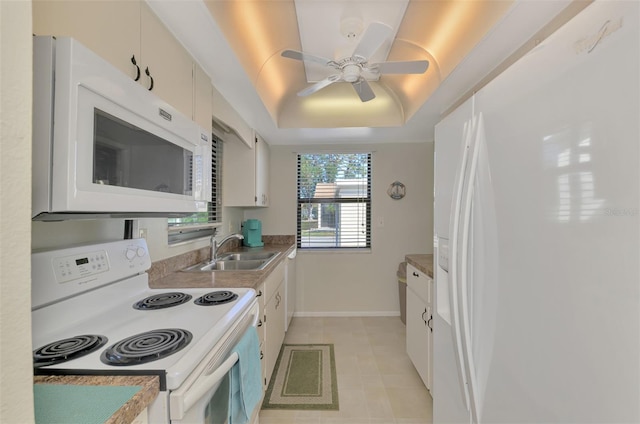 kitchen with white appliances, white cabinetry, a tray ceiling, and sink