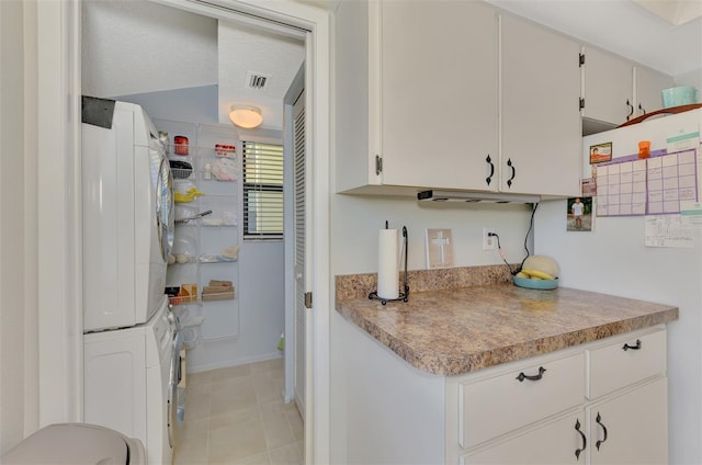 kitchen with stacked washing maching and dryer, light tile patterned flooring, and white cabinetry