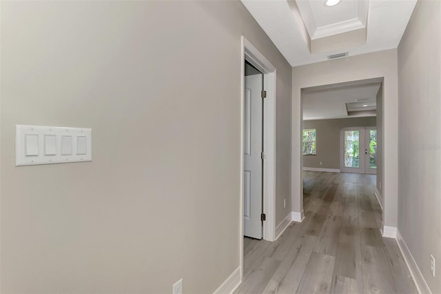 corridor featuring visible vents, baseboards, a raised ceiling, light wood-style flooring, and crown molding