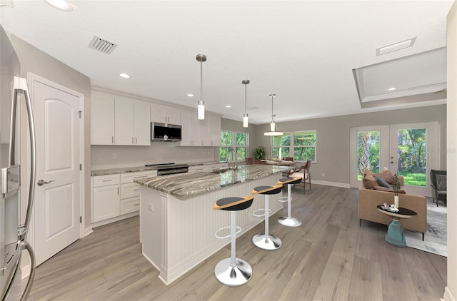 kitchen featuring a kitchen island with sink, stainless steel appliances, visible vents, white cabinets, and light stone countertops