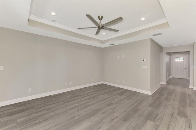 spare room featuring baseboards, a tray ceiling, and light wood-style floors