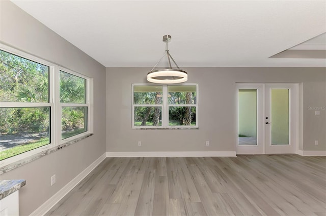 spare room featuring light wood-type flooring, plenty of natural light, baseboards, and french doors