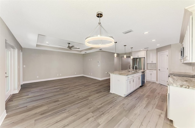 kitchen featuring a center island with sink, white cabinets, a raised ceiling, open floor plan, and decorative light fixtures