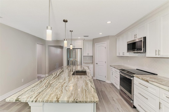 kitchen with white cabinets, an island with sink, stainless steel appliances, pendant lighting, and a sink