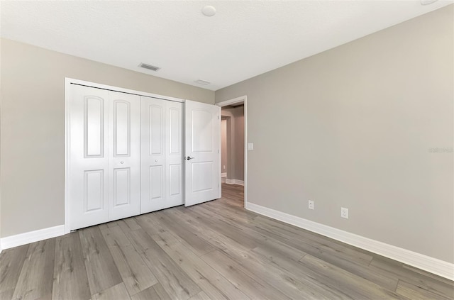 unfurnished bedroom with a textured ceiling, visible vents, baseboards, a closet, and light wood-type flooring