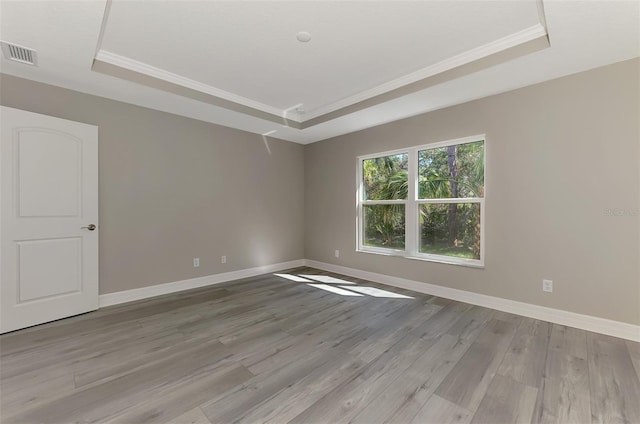 unfurnished room with light wood finished floors, visible vents, and a tray ceiling