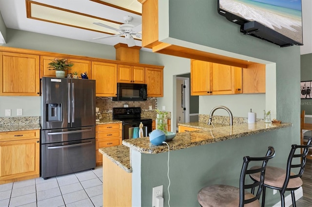 kitchen featuring tasteful backsplash, a sink, light stone countertops, a peninsula, and black appliances