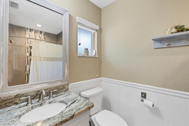 full bathroom featuring curtained shower, toilet, vanity, visible vents, and wainscoting