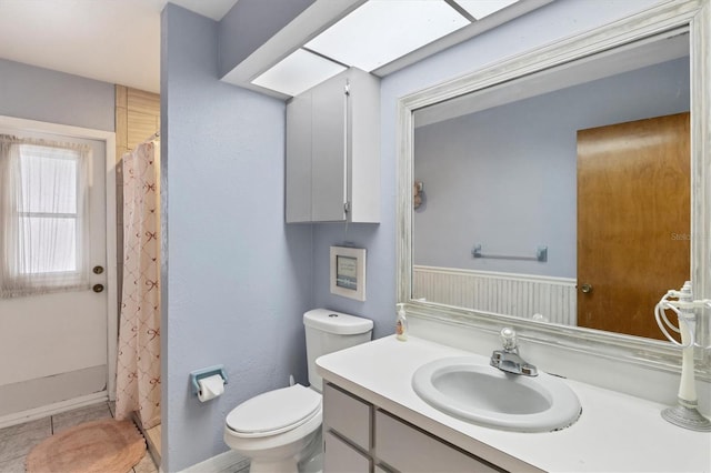 full bath featuring a skylight, a wainscoted wall, curtained shower, toilet, and vanity