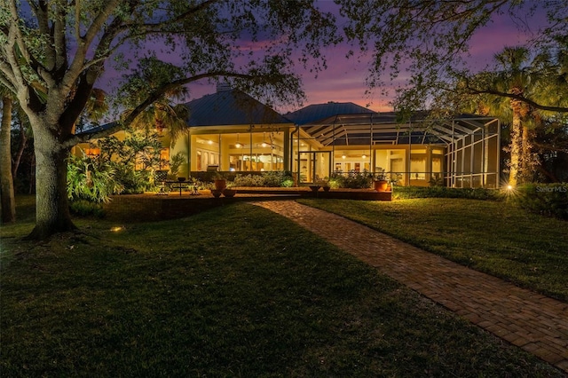 back house at dusk with a lawn, ceiling fan, and glass enclosure