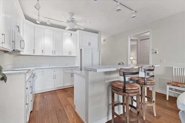 kitchen with light hardwood / wood-style flooring, a kitchen island, white appliances, white cabinets, and a kitchen breakfast bar