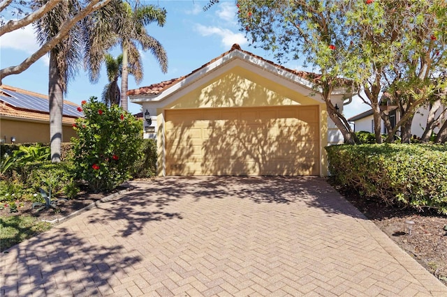 view of front facade featuring stucco siding, a tiled roof, decorative driveway, and a garage