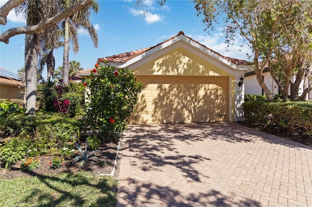 view of front of property featuring decorative driveway, a garage, a tile roof, and stucco siding