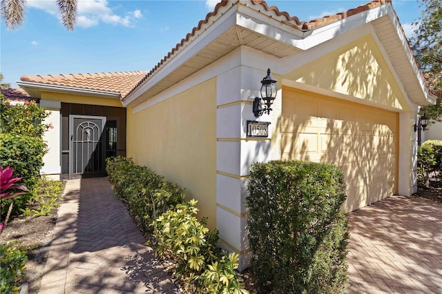 doorway to property with a tile roof, decorative driveway, a garage, and stucco siding