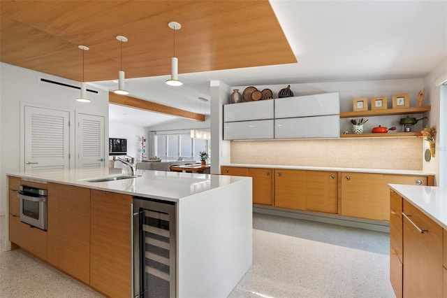 kitchen with stainless steel oven, vaulted ceiling, beverage cooler, sink, and a kitchen island with sink