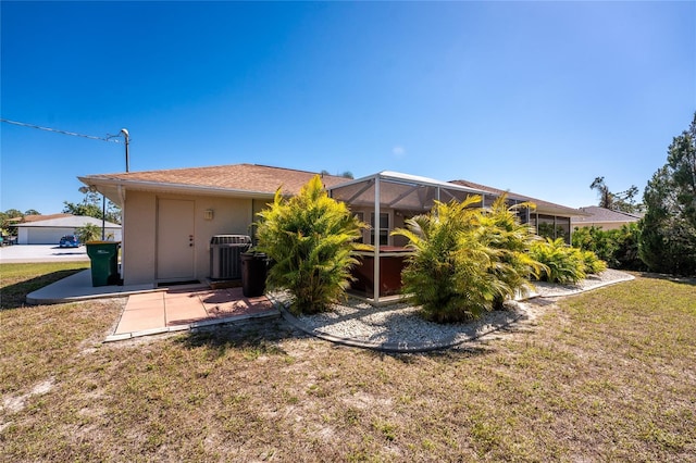 rear view of house with a lanai, a yard, central air condition unit, and stucco siding