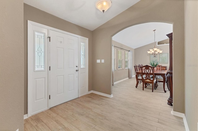 entrance foyer featuring arched walkways, a notable chandelier, light wood-style floors, vaulted ceiling, and baseboards