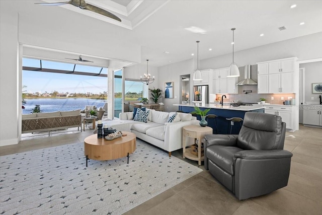 living room with light tile patterned floors, recessed lighting, ceiling fan with notable chandelier, a high ceiling, and a water view