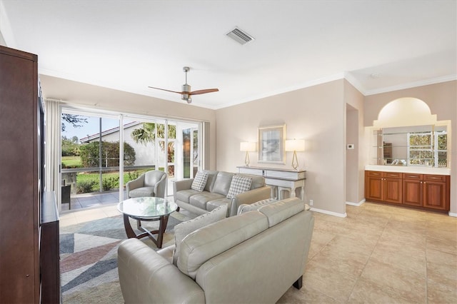 living room with light tile patterned flooring, a ceiling fan, visible vents, baseboards, and crown molding