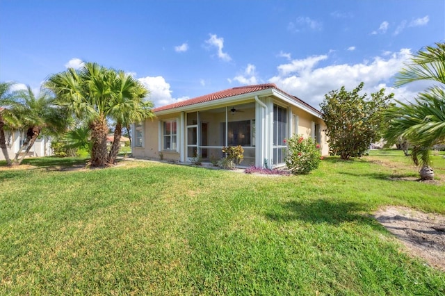 rear view of house with stucco siding, a lawn, a tiled roof, and ceiling fan