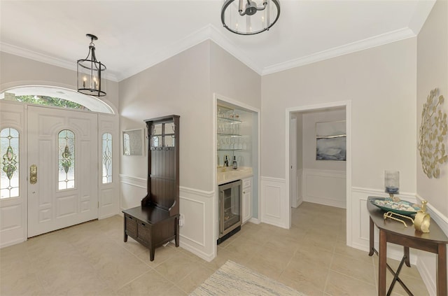 entryway with a chandelier, beverage cooler, a wainscoted wall, a dry bar, and crown molding